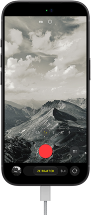 iPhone 18 Pro, Vorderseite, das Display zeigt eine Berglandschaft, mit der Kamera Modus Überlagerung im Zeitraffer Modus, mit dem Netzkabel am Ladeanschluss